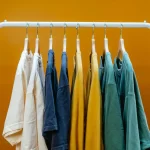 A sleek metal clothing rail in a high-end fashion boutique displaying identical premium garments organized smoothly by color variations.
